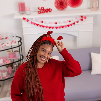Woman wearing heart shape head bopper and red sweater  in a festive living room.